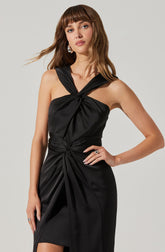 The woman is wearing a black satin dress with a sleeveless design. The dress features a twisted knot detail on the shoulder and a large gathered knot at the waist, creating a draped effect. The fabric has a smooth, shiny texture, and the dress has a slit on one side.